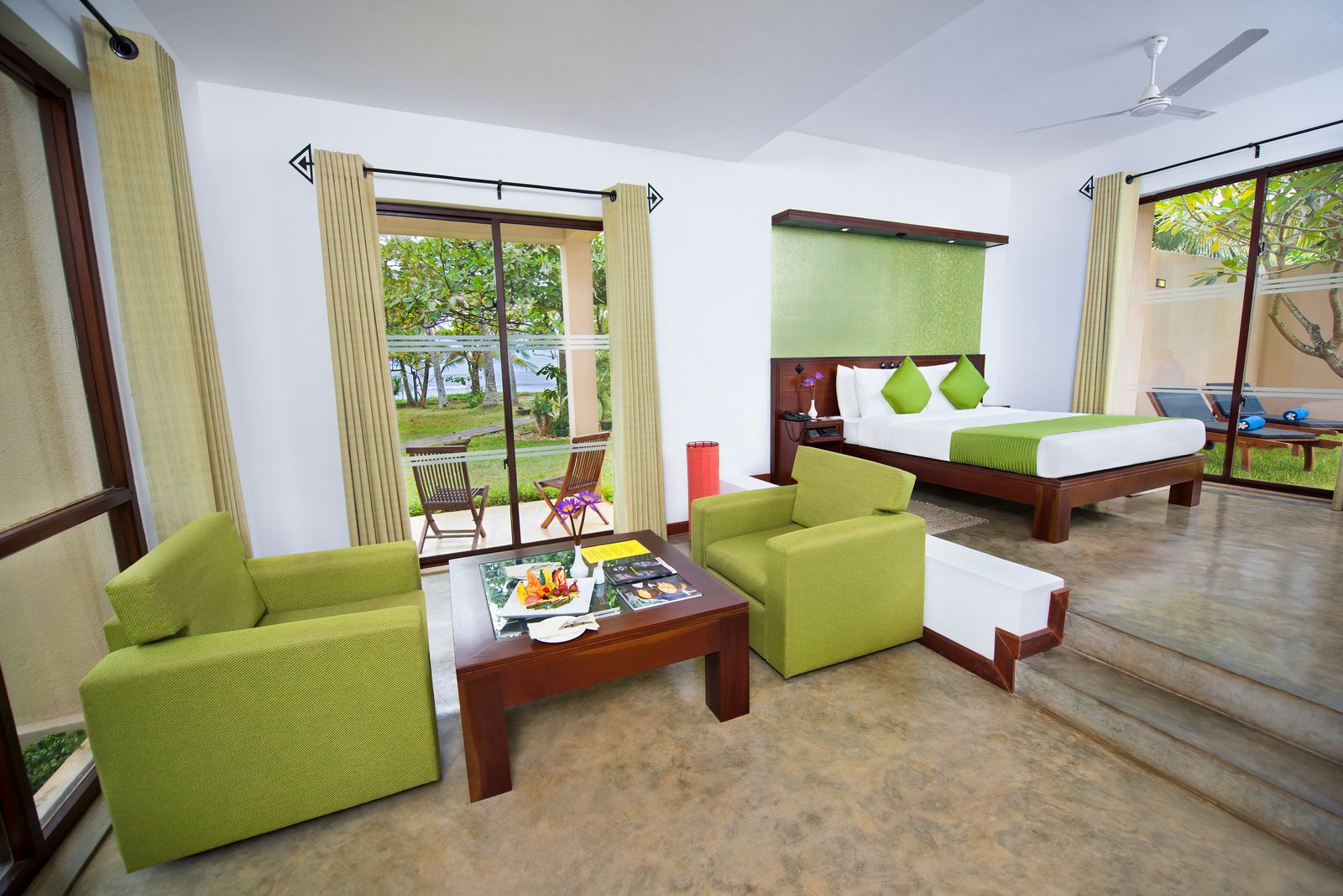 A Superior Room with Plunge Pool: a double bed with green cushions, 2 green armchairs round a low table, and glass doors to a porch facing palms and the sea